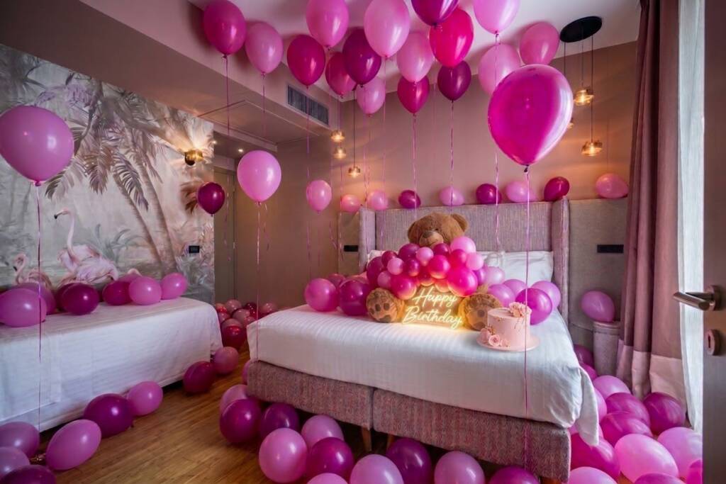 Room 23 at Hotel Duomo Firenze decorated for a pink birthday, with pink and fuchsia balloons, a giant teddy bear, a pink cake and a glowing Happy Birthday sign