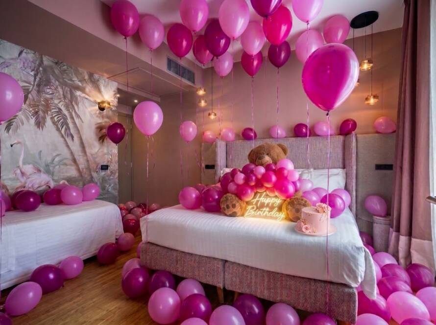 Room 23 at Hotel Duomo Firenze decorated for a pink birthday, with pink and fuchsia balloons, a giant teddy bear, a pink cake and a glowing Happy Birthday sign