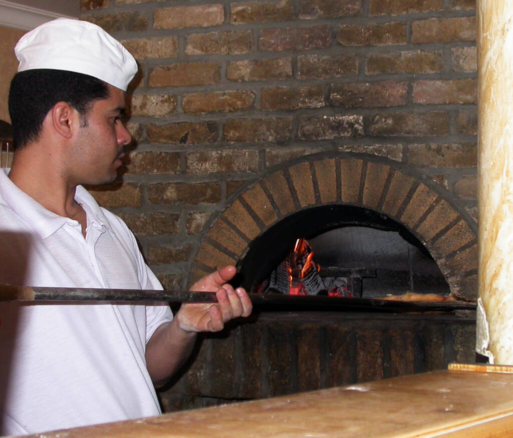 Pizzaiolo che inforna una pizza nel forno a legna